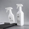 A white spray bottle with a pump dispenser is shown on a dark surface, ready for refillable plastic spray bottle use.