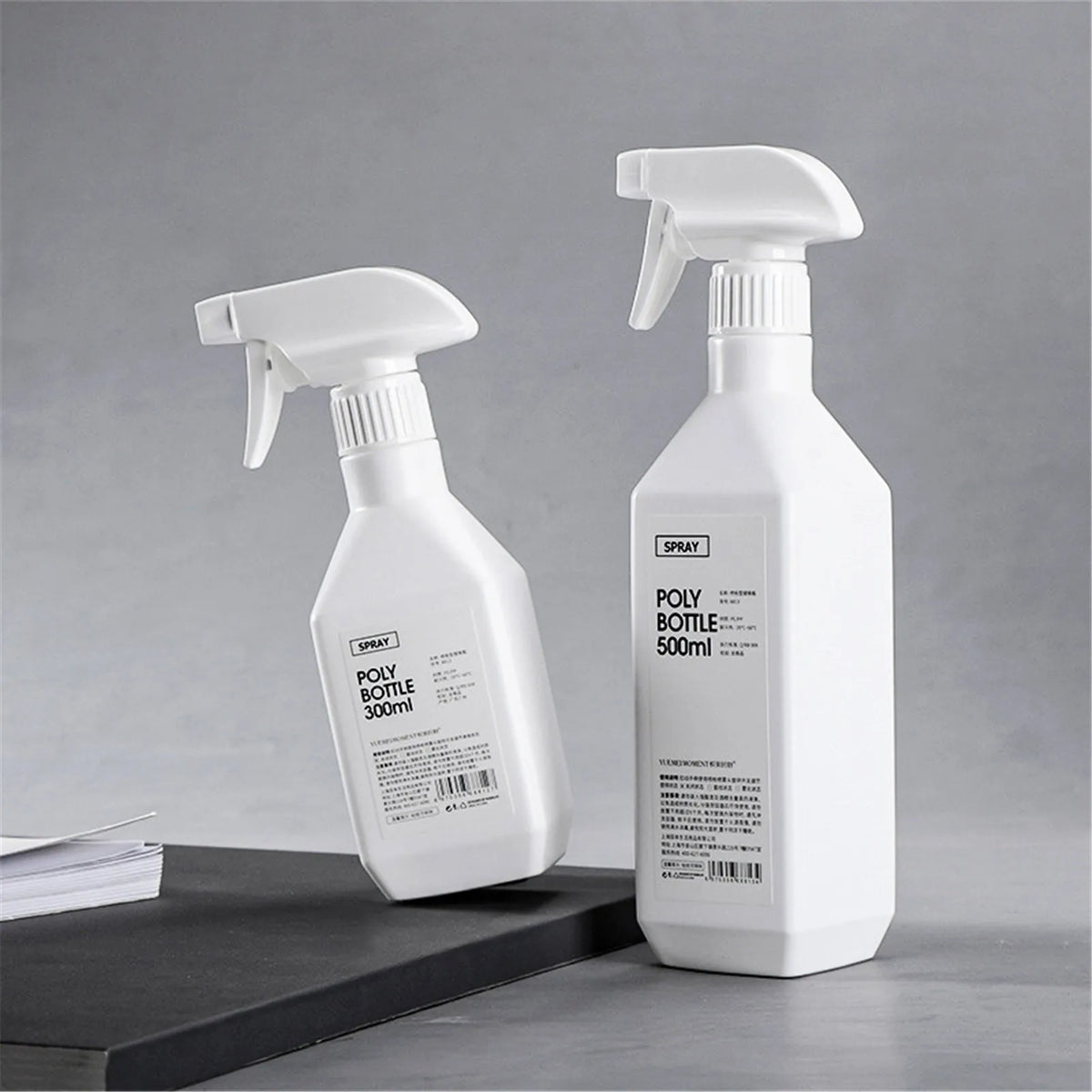 A white spray bottle with a pump dispenser is shown on a dark surface, ready for refillable plastic spray bottle use.