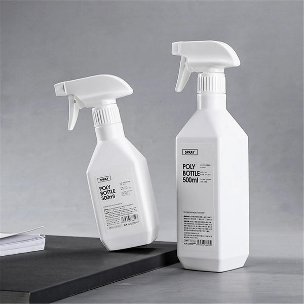 A white spray bottle with a pump dispenser is shown on a dark surface, ready for refillable plastic spray bottle use.