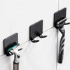 A black aluminum shaving razor storage rack mounted on a white tiled wall.