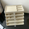 A clear acrylic 5-tier desktop jewelry organizer rack with light beige compartments and silver-toned jewelry stands.