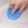 Una mano sostiene una esponja de limpieza natural azul brillante en agua jabonosa.