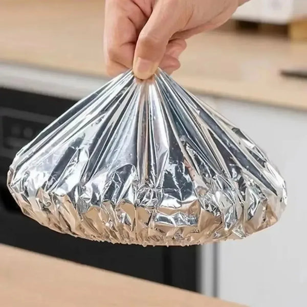 A hand is holding a crinkled reusable aluminum foil bowl cover for food preservation.