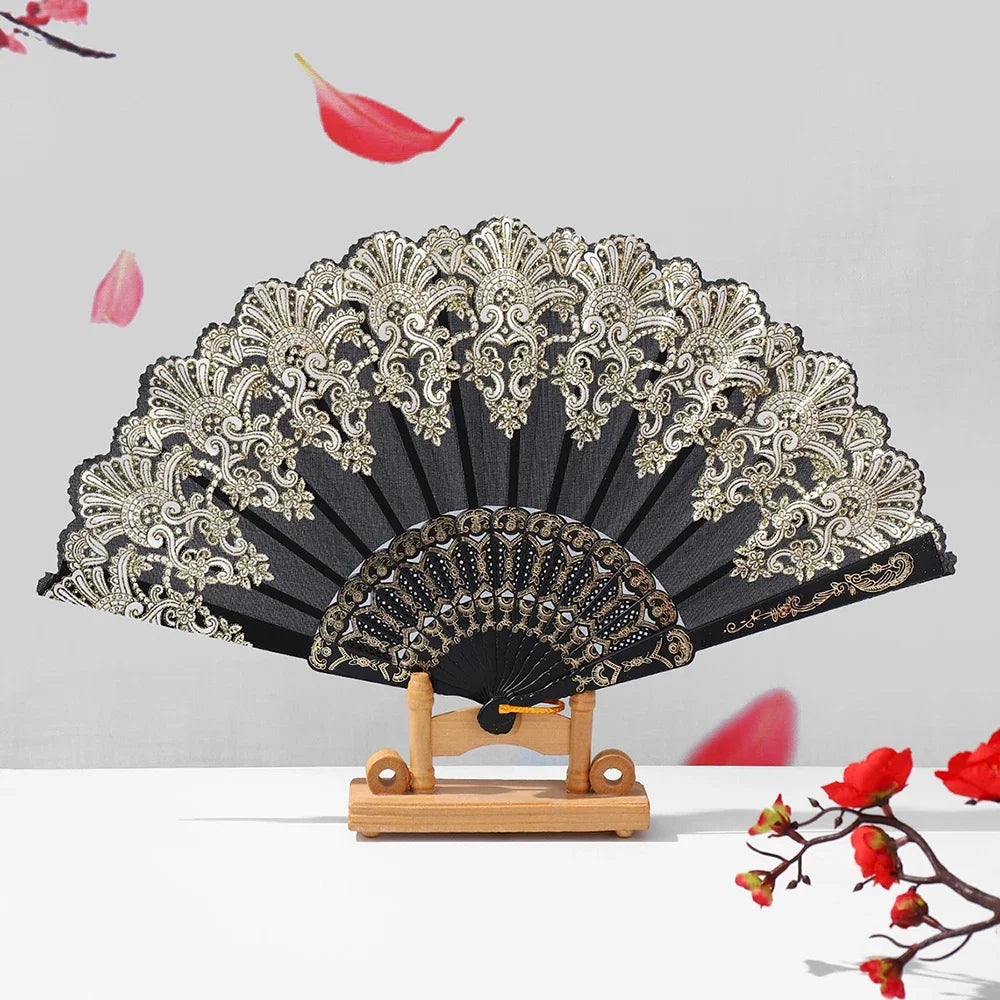A black and gold ornate folding hand fan with intricate detailing displayed against a light gray background.