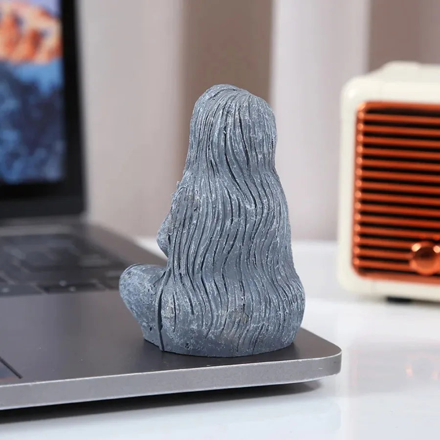 A gray resin statue of a long, wavy-haired figure resembling a moon goddess placed on a laptop.