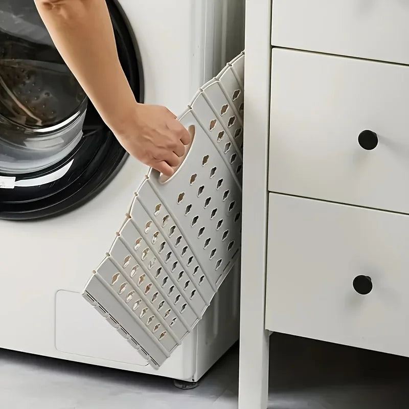 A hand is inserting small clothes into a folding hand-held clothes storage basket inside a white cabinet drawer.
