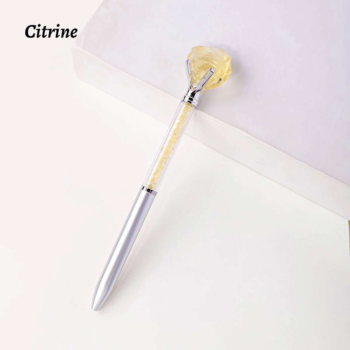 A gold-colored crystal is held by a silver pen, displayed on a white background.