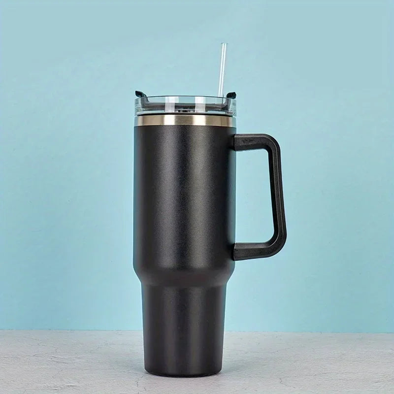 A black insulated stainless steel tumbler with a handle and straw is shown against a light blue background.