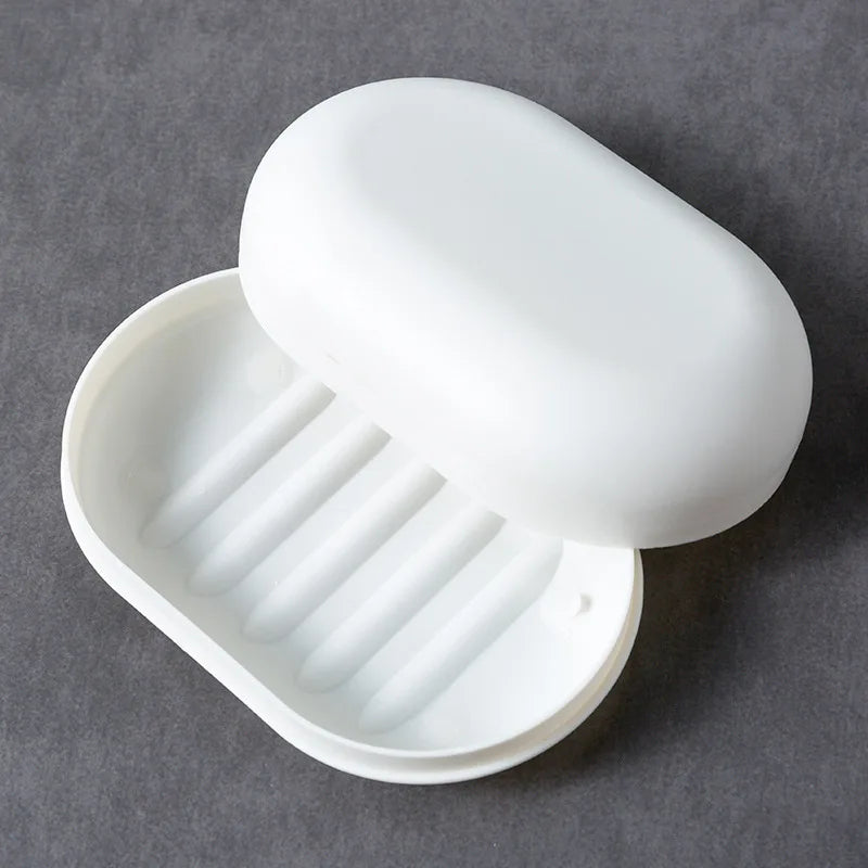 A white portable soap holder with a lid is shown open, displaying ribbed compartments for holding soap.