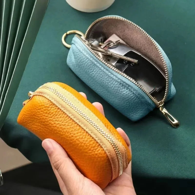 A hand holds an orange leather key organizer wallet next to a light blue leather zipper wallet on a green surface.