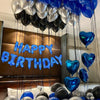 Blue heart balloons and silver balloons are suspended in a vertical arrangement for a birthday decoration.