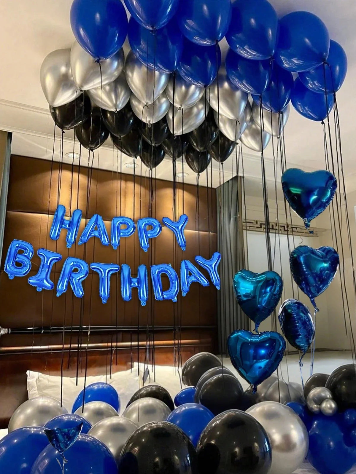 Blue heart balloons and silver balloons are suspended in a vertical arrangement for a birthday decoration.