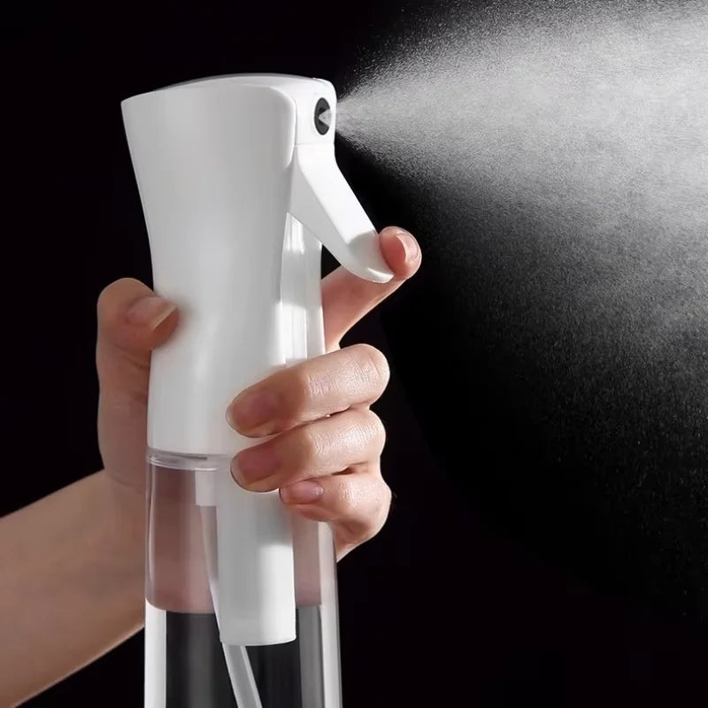 A hand is holding a white refillable continuous spray bottle and spraying mist onto a dark surface.