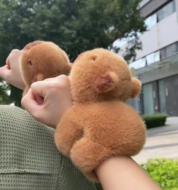 A person is holding a small, fluffy, brown capybara-like plush toy against their hand.