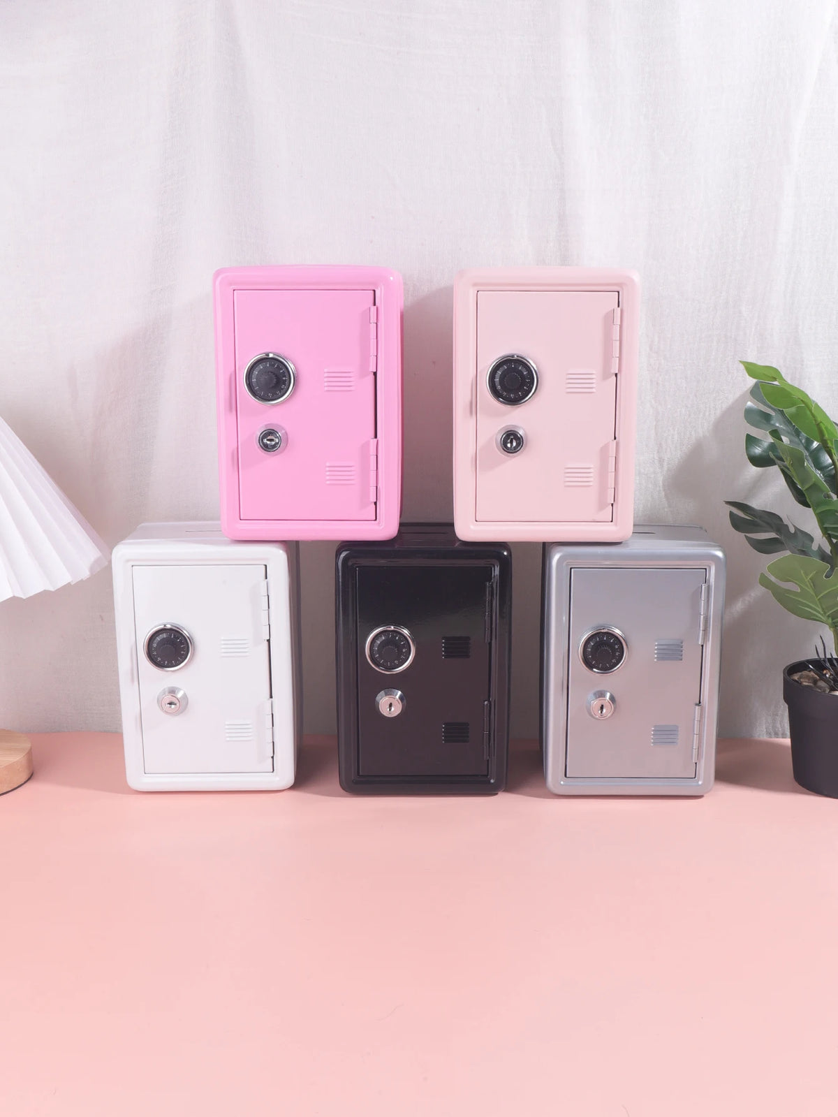 A set of four solid color metal piggy banks in pink and gray tones displayed on a light surface.