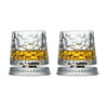 Un par de vasos de whisky transparentes y texturizados con líquido de color dorado y bases plateadas.