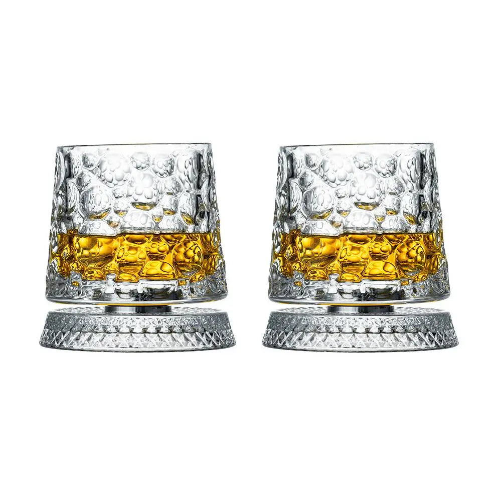 Un par de vasos de whisky transparentes y texturizados con líquido de color dorado y bases plateadas.