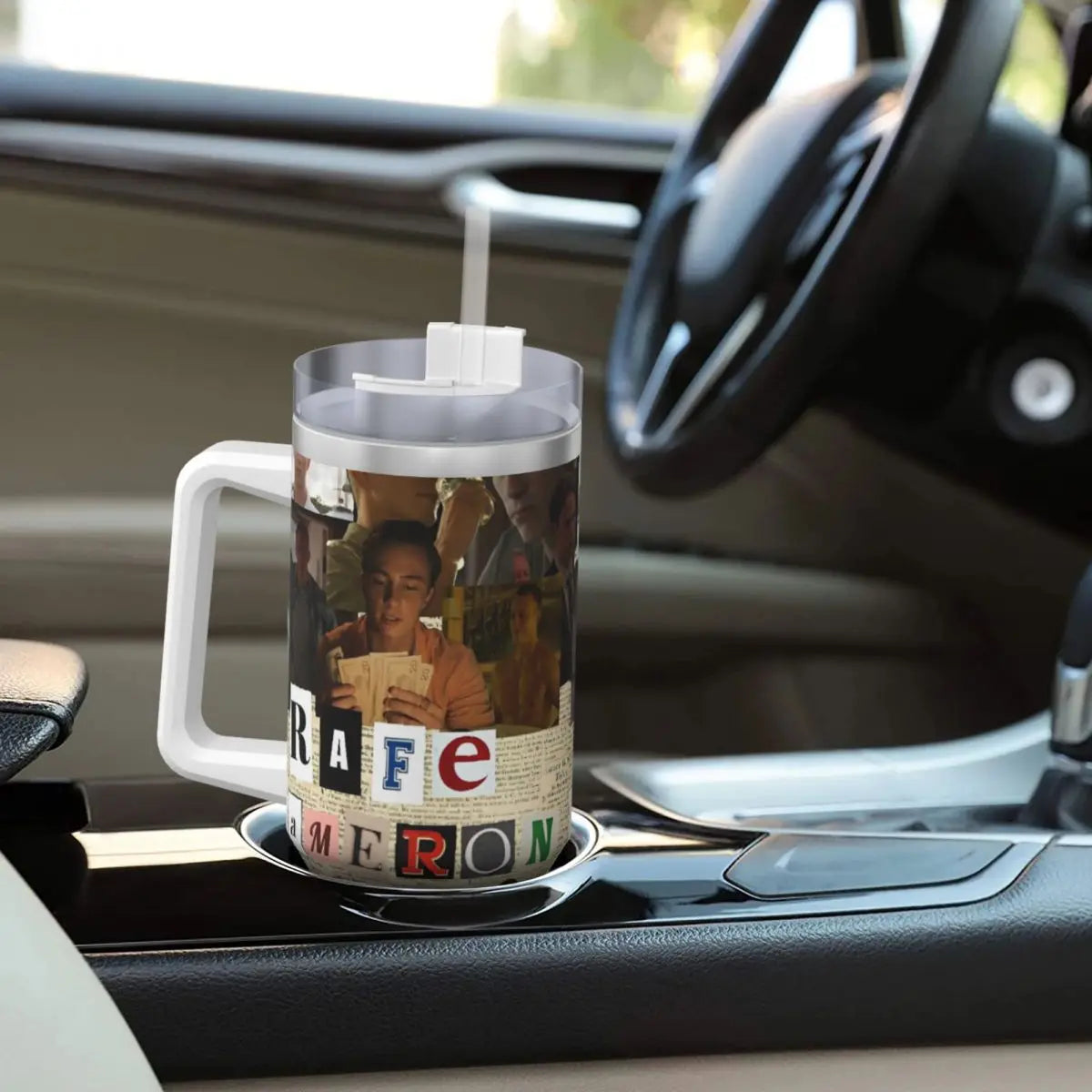 A stainless steel travel tumbler mug with a printed design featuring a person and text is resting on a car dashboard.