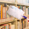 A hand is using a white reusable duster refill on a shelf filled with books.