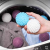 A hand is holding a light blue and white reusable laundry ball inside a washing machine drum.