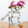 A glass jar filled with water and pink lotus flowers, featuring crystal crushed ice stones for decor.