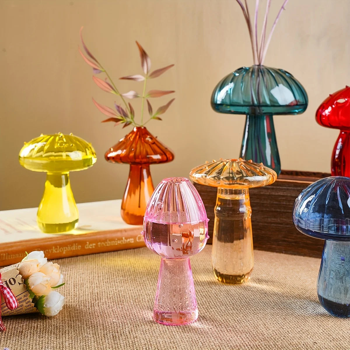 A collection of glass mushroom-shaped vases and decorative items in various colors like yellow, orange, pink, and blue on a t