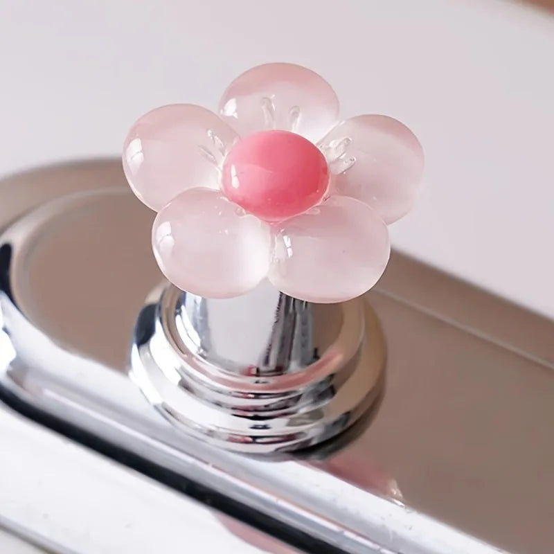 A flower-shaped toilet flush button with pink and white translucent petals on a chrome base.