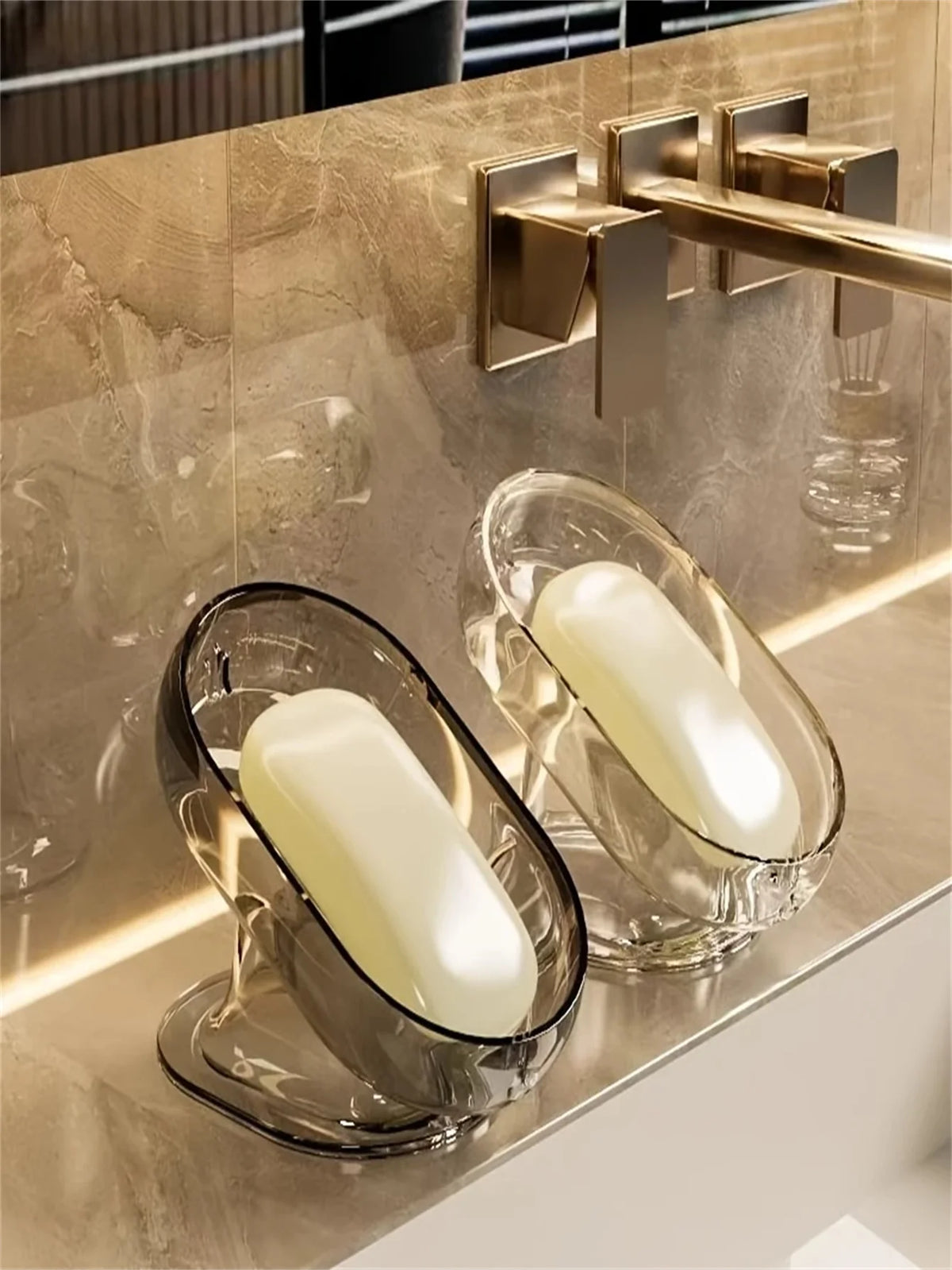 A clear glass soap dish holding a white bar of soap on a modern bathroom countertop.
