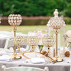 A gold crystal tealight candlestick candelabra set displayed on a white table with pink flowers and greenery.