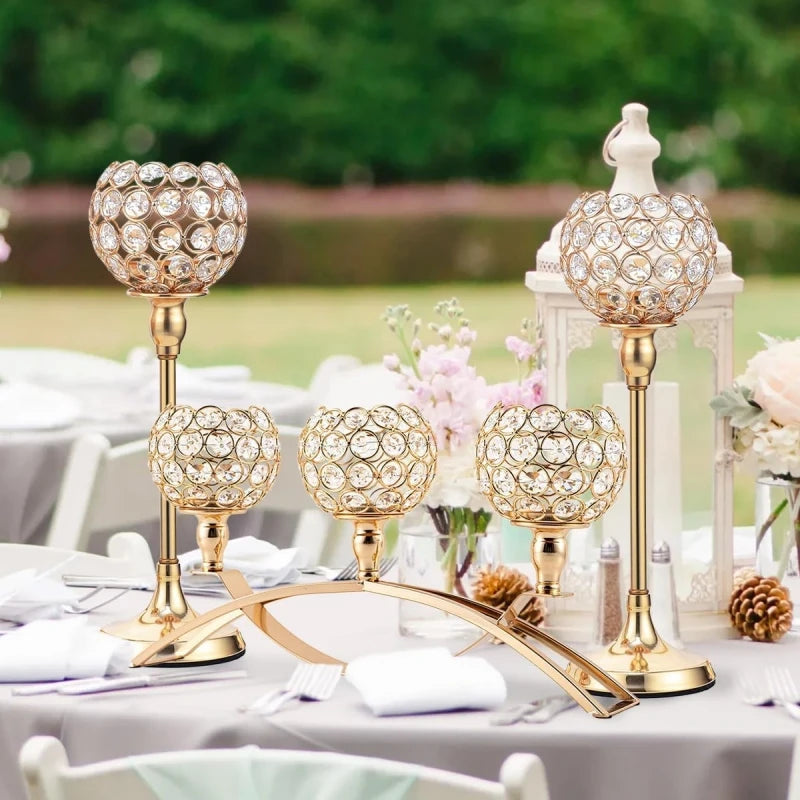 A gold crystal tealight candlestick candelabra set displayed on a white table with pink flowers and greenery.