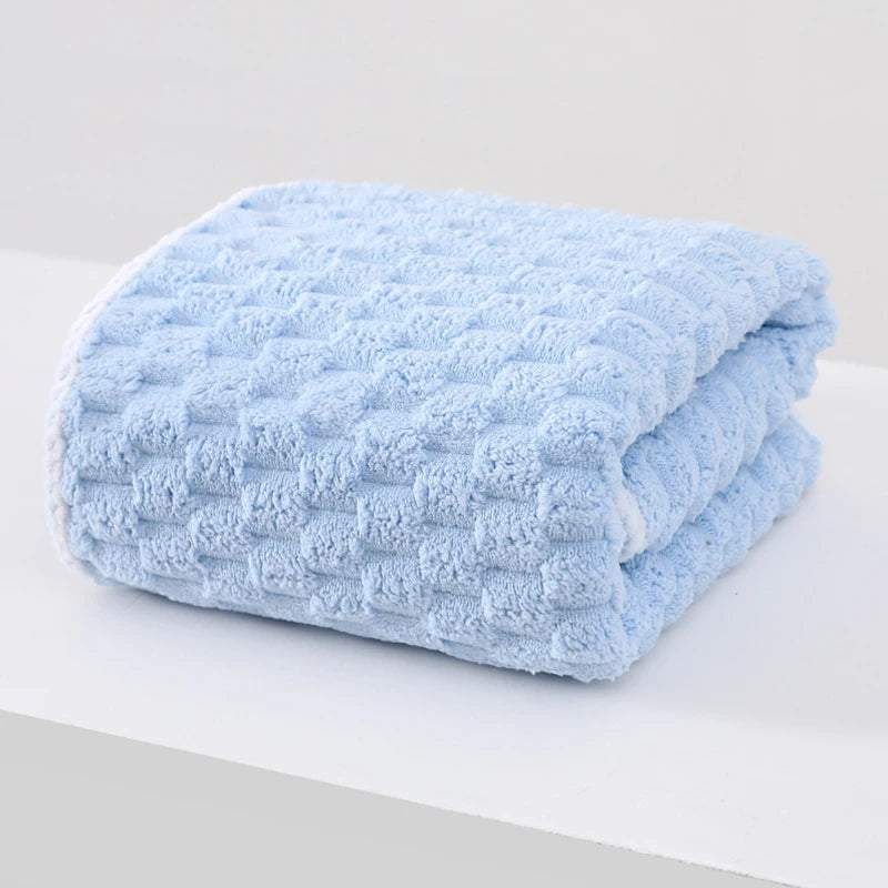 A light blue thickened microfiber bath towel folded on a white surface.