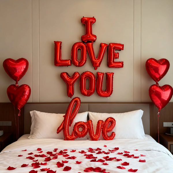 Rote Folienballons mit 'I love you' und 'love' auf einem Bett mit roten Rosenblättern