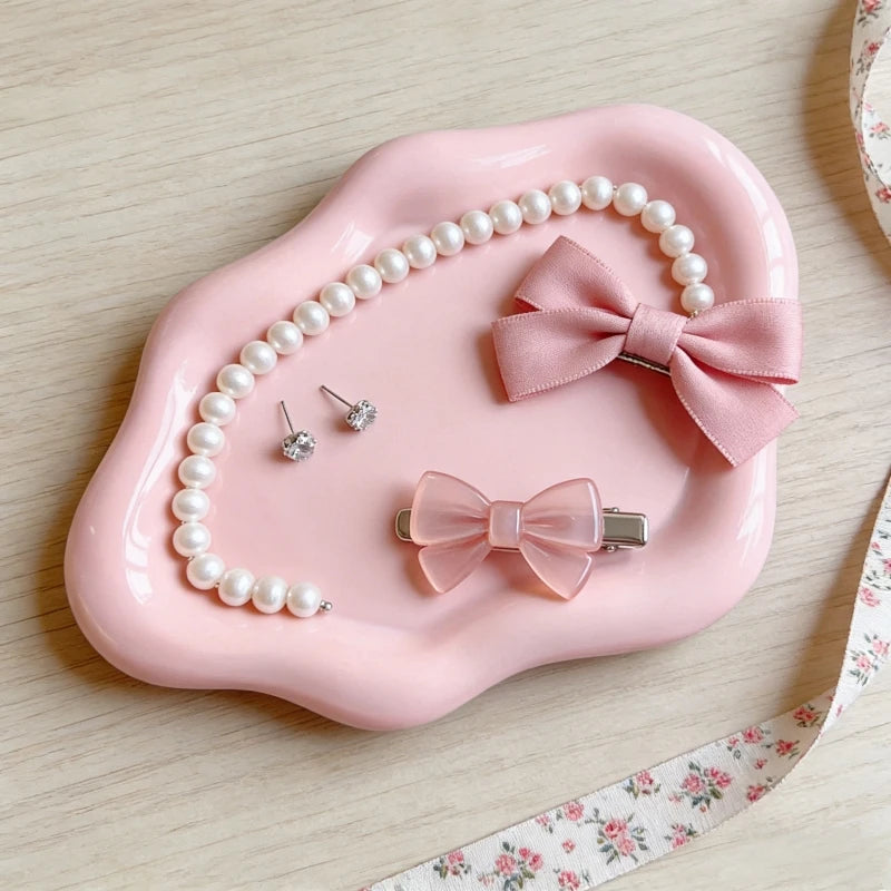 A pink cloud-shaped jewelry organizer tray holding pearl strands and a bow-shaped earring.