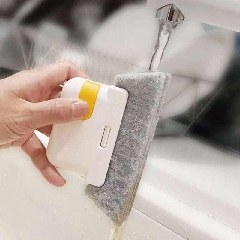 Una mano usa un cepillo de limpieza blanco y amarillo para limpiar una riel de ventana.