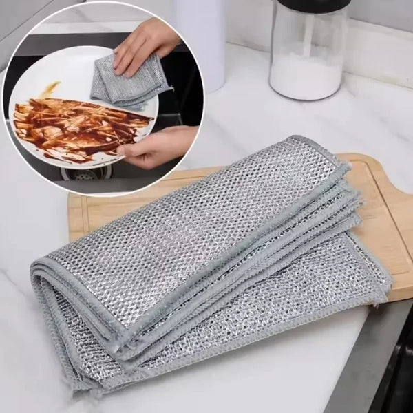 A set of gray thickened steel wire cleaning cloths is shown being used to clean food on a white plate.