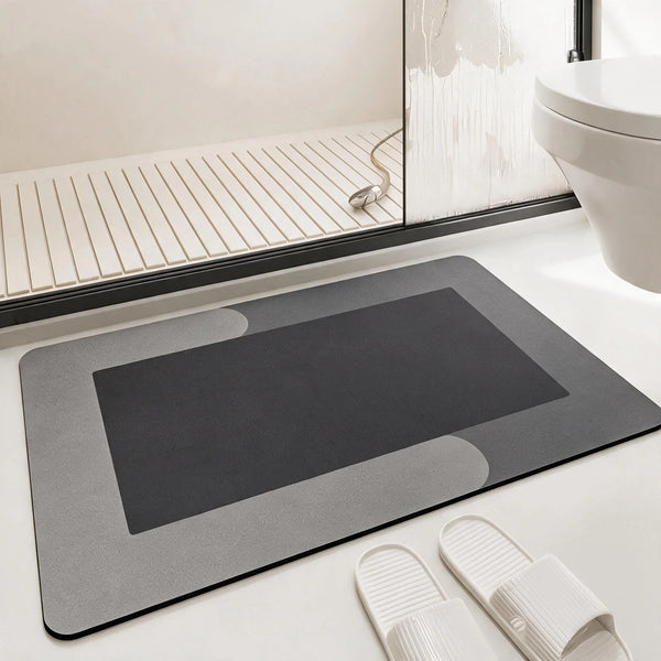 A rectangular gray bath mat with a dark inset and non-slip rubber backing is shown on a white surface.