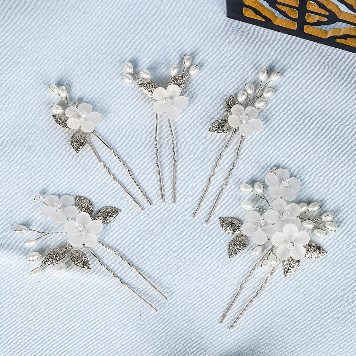A set of silver pearl flower bridal hair clips displayed on a light blue background.