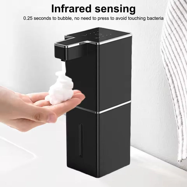 A hand is dispensing soap into a wall-mounted touchless automatic soap dispenser with infrared sensing.