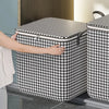 A hand is opening a black and white checkered non-woven quilt storage box with a clear window.