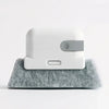 A white cleaning brush with a gray section rests on a gray, textured mat.