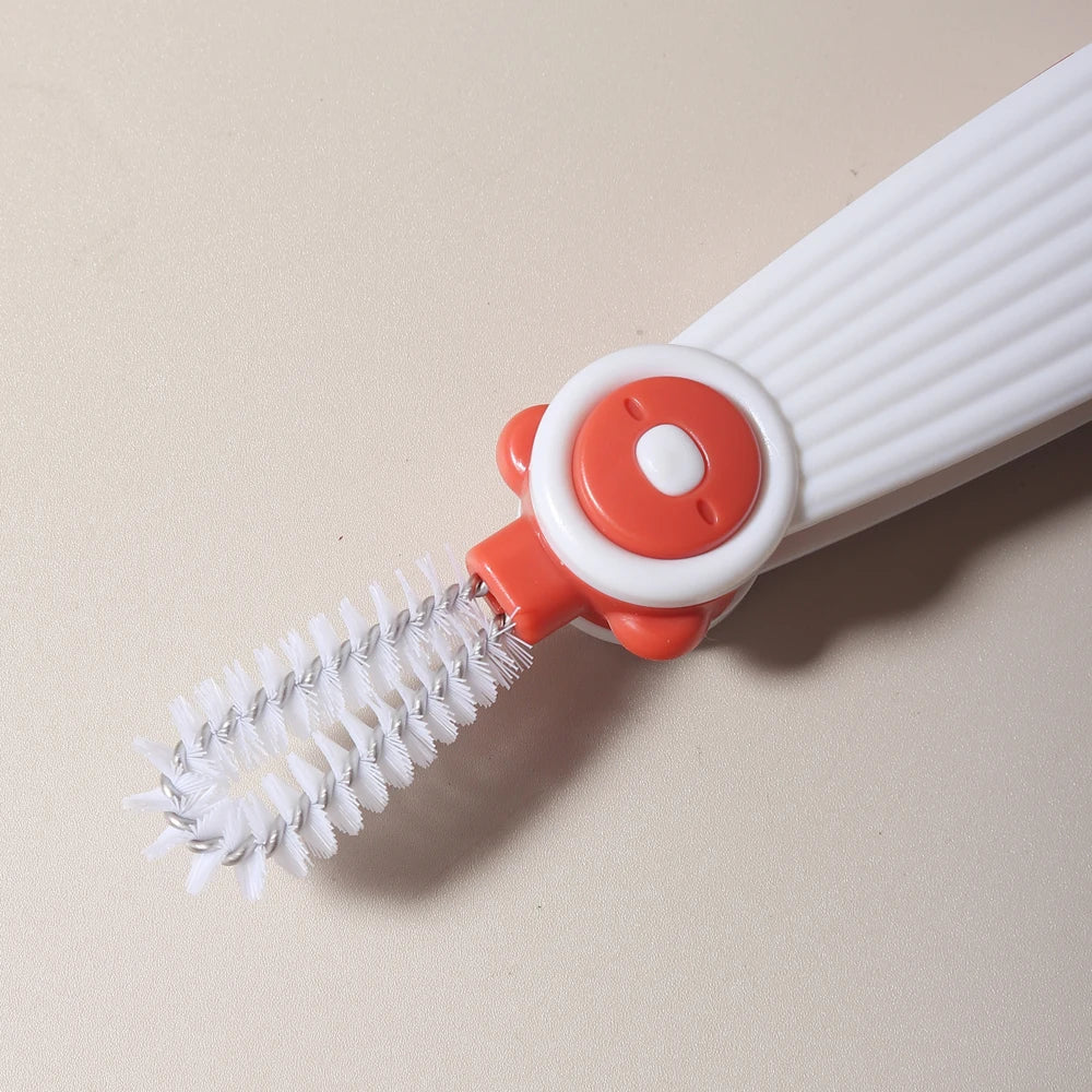 A white silicone baby bottle cleaning brush with an orange grip and bristles is shown against a light background.