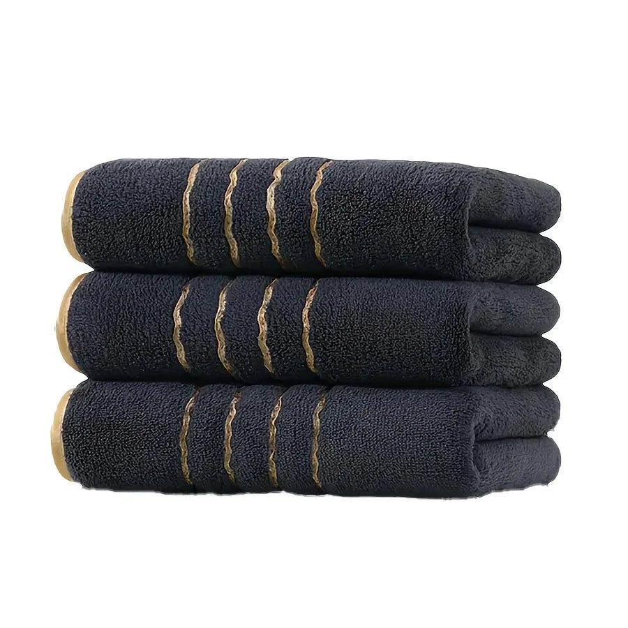A stack of black coral fleece towels with gold stripe detailing.