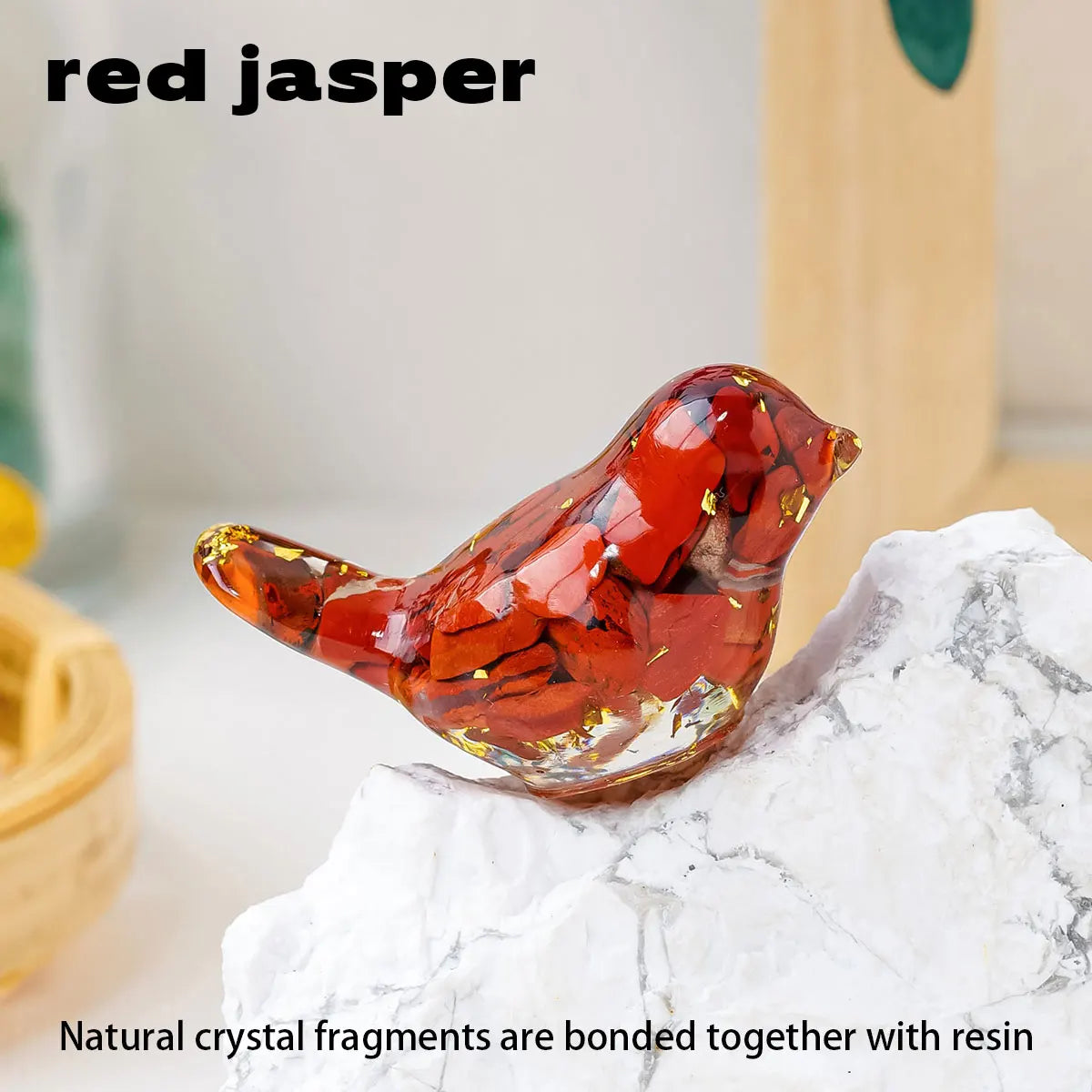 A small, reddish-orange crystal bird statue made from natural crystal fragments and resin resting on a white rock.