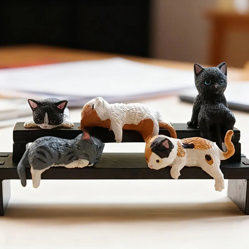 A set of five cute healing cat figurines in various colors and patterns arranged on a dark wooden surface.