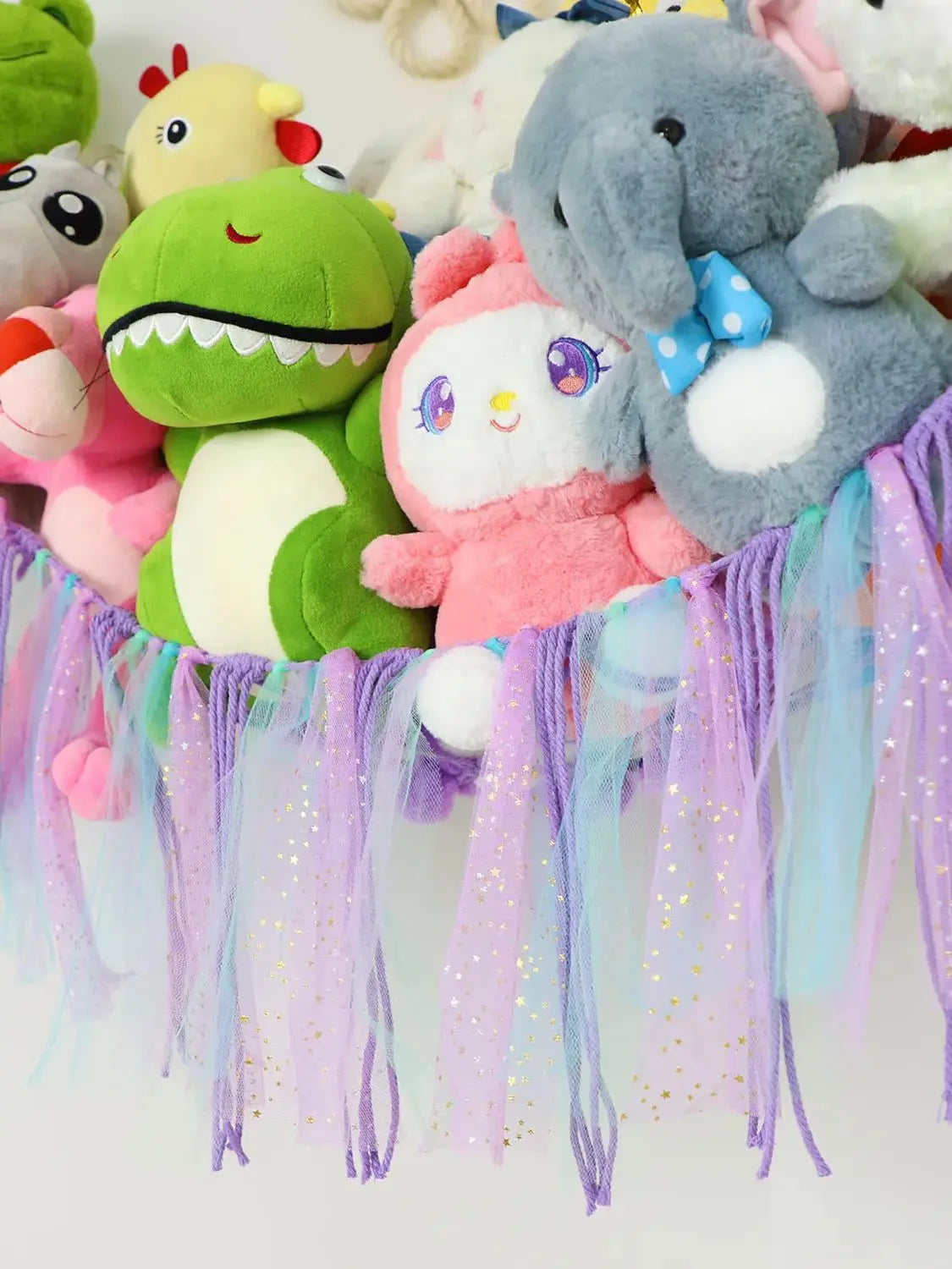 A colorful bohemian stuffed animal hammock featuring plush toys in pastel colors and purple, pink, and blue streamers.