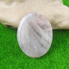 A smooth, translucent white quartz thumb stone resting on green grass.