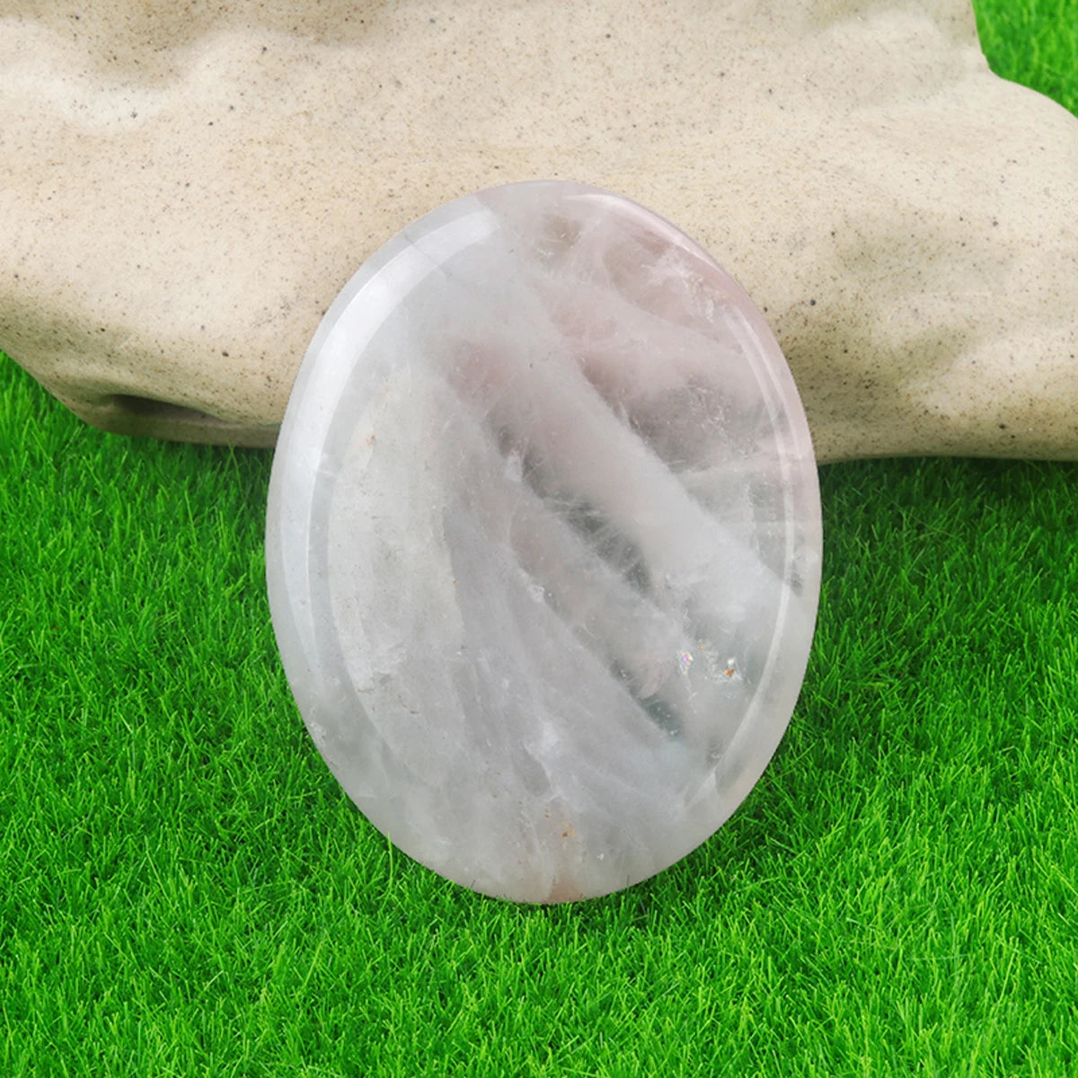 A smooth, translucent white quartz thumb stone resting on green grass.