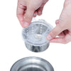 A hand is placing a disposable sink drain filter bag over a metal strainer for filtration.