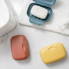 A collection of portable travel soap boxes in pink, white, and yellow are displayed on a white surface.