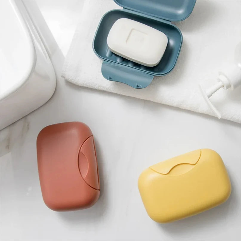 A collection of portable travel soap boxes in pink, white, and yellow are displayed on a white surface.